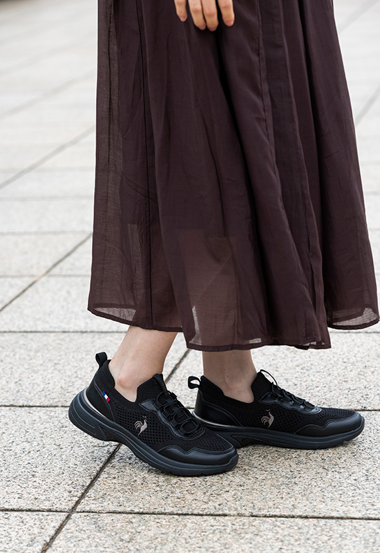落ち着いたカラーのオフィスファッションに馴染む黒のワイド設計スニーカーとリュックスタイル