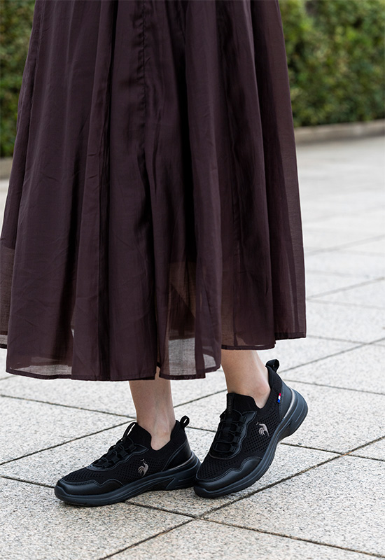落ち着いたカラーのオフィスファッションに馴染む黒のワイド設計スニーカーとリュックスタイル