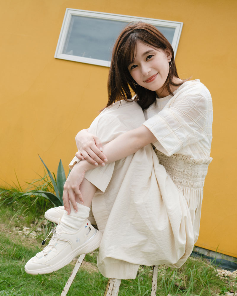 ルコックスポルティフのサマースニーカーを履いて軽やかに歩く芳根京子さん。スカートとソックスを合わせた大人のきれいめ夏コーデ。ベージュカラーのスニーカーサンダル