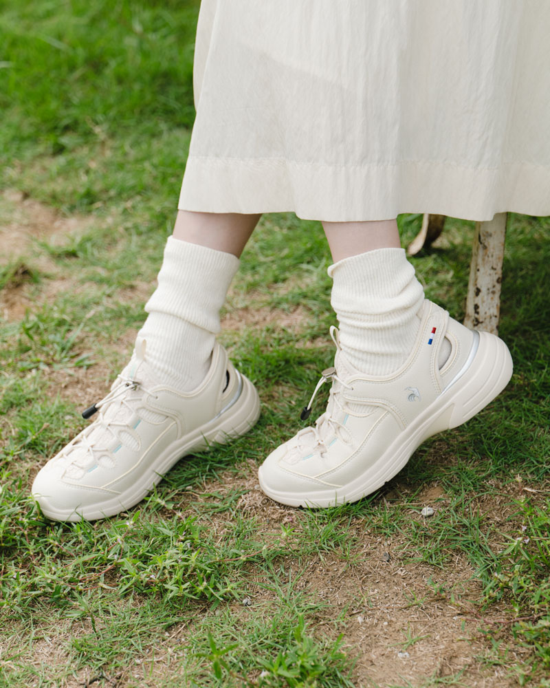 ルコックスポルティフのサマースニーカーを履いて軽やかに歩く芳根京子さん。スカートとソックスを合わせた大人のきれいめ夏コーデ。ベージュカラーのスニーカーサンダル