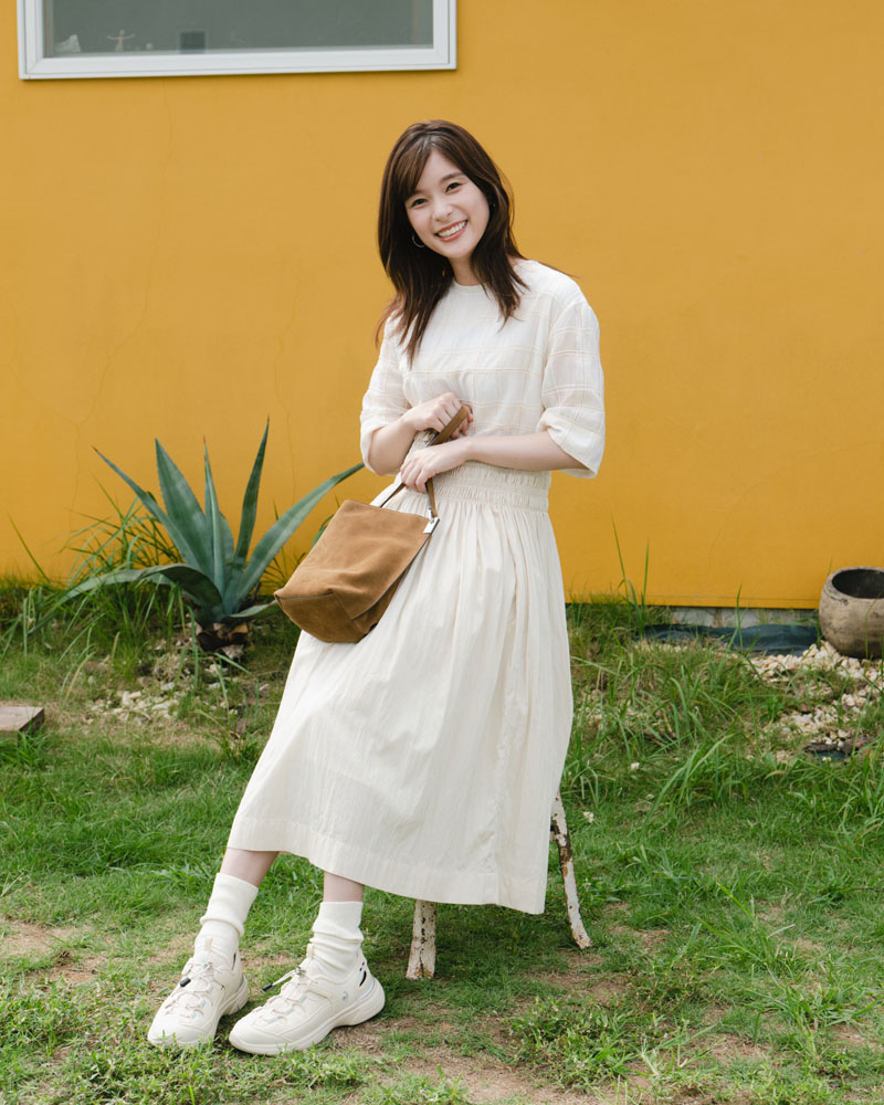 ルコックスポルティフのサマースニーカーを履いて軽やかに歩く芳根京子さん。スカートとソックスを合わせた大人のきれいめ夏コーデ。ベージュカラーのスニーカーサンダル