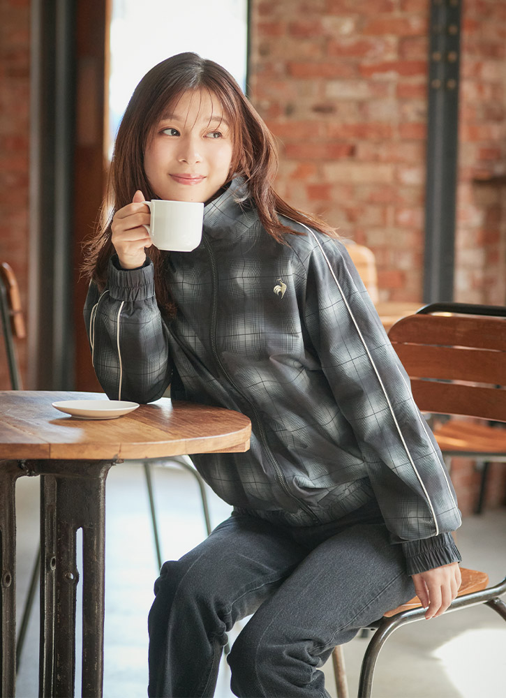 カフェでシックなチェック柄のグラフィックウィンドジャケットを着て寛ぐ芳根京子さん